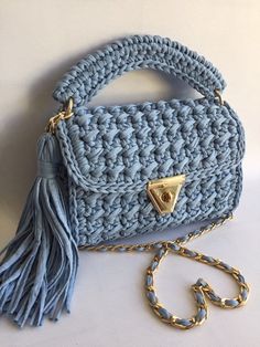 a crocheted purse with a tasseled handle and gold tone hardware, on a white surface