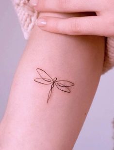 a woman's arm with a small dragonfly tattoo on it