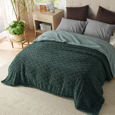 a bed with a green blanket on top of it next to a night stand and potted plant