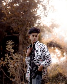 a young man is standing in front of some trees and bushes wearing a jacket with letters on it