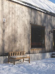 a wooden bench sitting in front of a building covered in snow next to a window