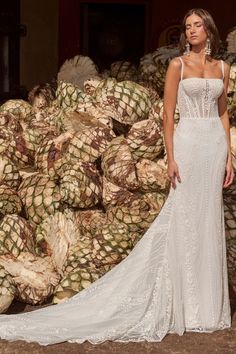 a woman standing in front of piles of pineapples wearing a wedding dress with spaghetti straps