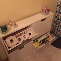 an open drawer with toilet paper and other items in it next to a shower curtain