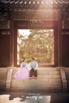 a man and woman sitting on the steps in front of a building with an open doorway