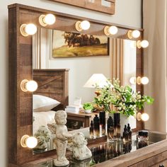 a mirror with some lights on top of it next to a dresser and vase filled with flowers