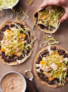 three pita breads topped with meat, cheese and veggies next to a bowl of sauce