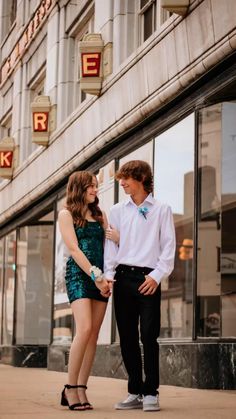 a young man and woman standing next to each other in front of a building