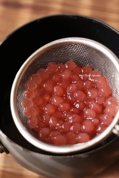 a metal strainer filled with red food on top of a wooden table next to a knife