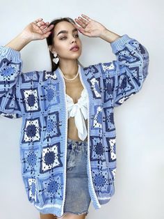 a woman is posing with her hands on her head and wearing a blue crocheted cardigan