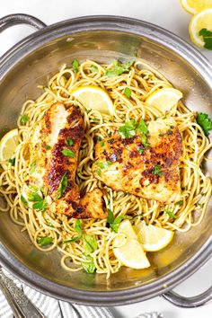 a pan filled with chicken and noodles next to lemon wedges