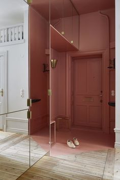 an empty hallway with pink walls and wooden flooring is seen through a glass door