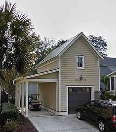 a garage with two cars parked in front of it and palm trees around the driveway