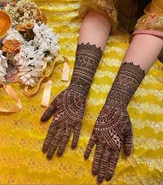 two hands with henna tattoos on them sitting next to flowers and ribboned table cloth