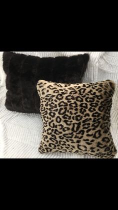 two pillows on top of a bed with white sheets and black fur trimmings