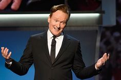 a man in a suit and tie standing on stage with his hands out to the side