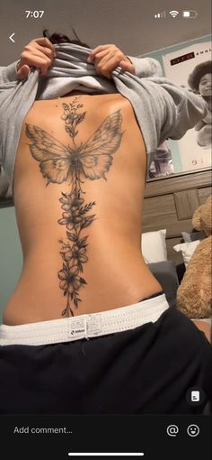 the back of a woman's body with flowers and a butterfly tattoo on it