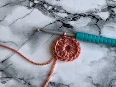 the crochet hook is laying on top of the marble floor next to an orange yarn ball