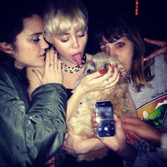 three women are taking pictures with their cell phones and one is holding a small dog