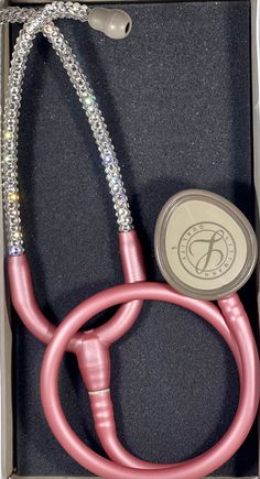 a pink stethoscope in a box with its lid open and some beads around it