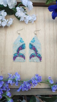 the beaded earrings are on display next to purple flowers and blue hydranges