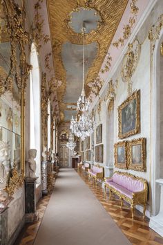 an ornate hallway with gold and white decor on the walls, chandeliers and paintings