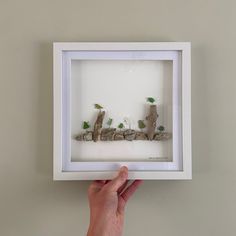 a person holding up a frame with small rocks and plants in it that spell out the word love