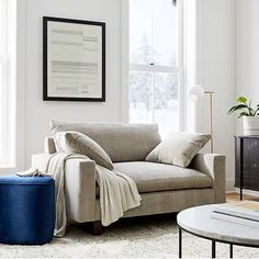 a living room with a couch, coffee table and ottoman in front of a window