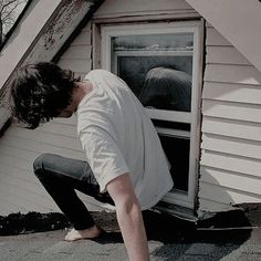 a man leaning against the side of a house with his head in an open window