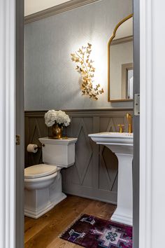 a white toilet sitting next to a sink in a bathroom under a mirror on top of a wooden floor