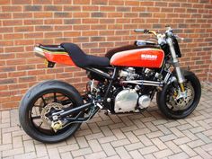 an orange and black motorcycle parked next to a brick wall