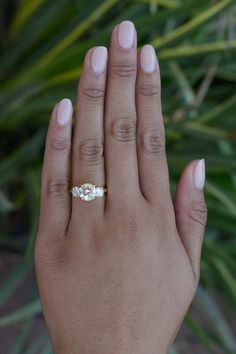 a woman's hand with a diamond ring on her left hand and palm trees in the background