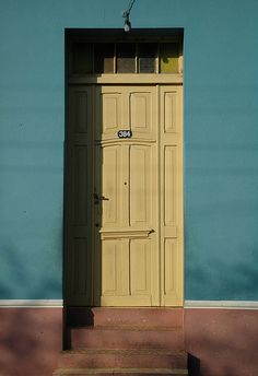 a yellow door on the side of a blue building with steps leading up to it