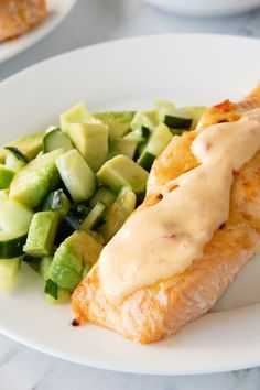 a white plate topped with salmon and cucumber next to a bowl of dressing