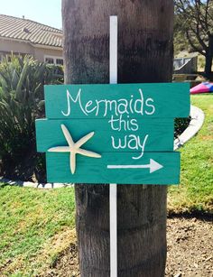 a wooden sign that says mermaids this way on the side of a palm tree