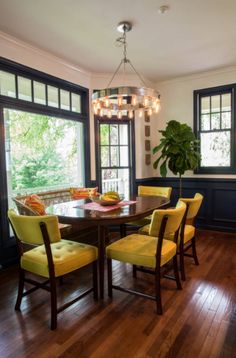 a dinning room table with yellow chairs in front of large windows and wood flooring