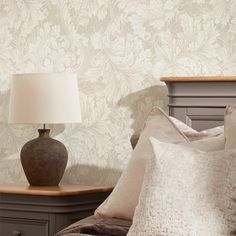 a lamp on a nightstand next to a bed with white pillows and a gray headboard