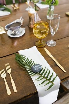 the table is set with silverware, gold cutlery and fern leaf napkins