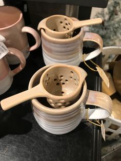 three ceramic cups with spoons in them sitting on a table next to other coffee mugs