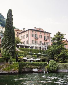 a large pink building sitting on top of a lush green hillside next to a body of water