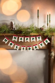 a happy holidays banner hanging from a mantle with candles and pine cones on it in the background