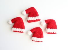 three red and white felt santa hats on a white surface with one hat in the middle