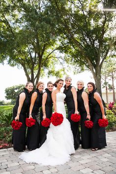 a group of women standing next to each other in black dresses and holding red flowers