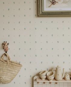 a basket is hanging on the wall next to a shelf with cups and vases