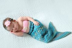 a baby girl wearing a blue and pink knitted mermaid tail sleeping on a white blanket