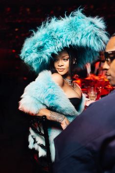 a woman in a blue fur hat and dress standing next to a man at a table