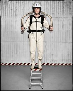 a man standing on top of a step ladder wearing a space suit and holding two hands