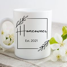 a white coffee mug with the name homeowner on it next to some flowers