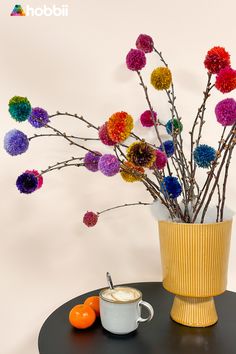 there is a vase with colorful pom - poms on the table next to an orange and coffee cup