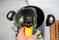 a person is holding a thermometer in front of a pot with cooking utensils