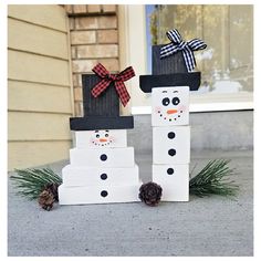 two snowmen made out of cardboard boxes sitting on the front porch with pine cones